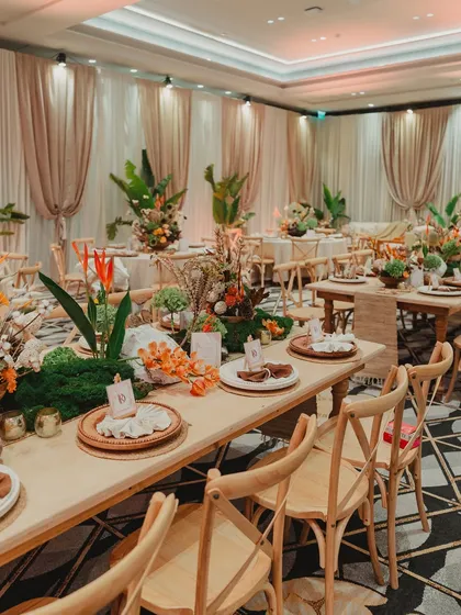 The dining setup for the carnival event, featuring long wooden tables, cross-back chairs, and lush, tropical-inspired centerpieces.