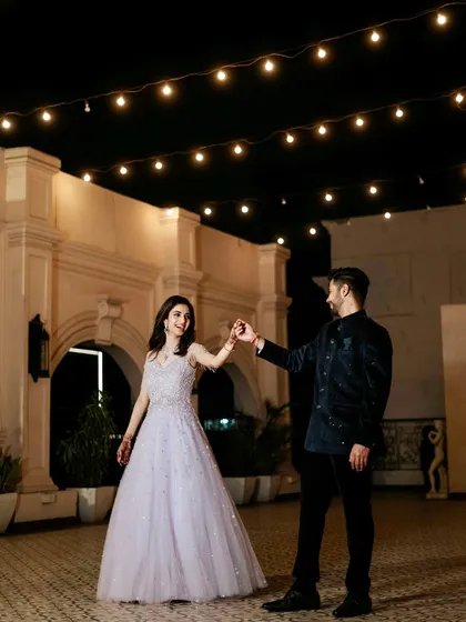 A fairytale dance under a canopy of string lights. This wide shot captures the romance of the location and the elegance of the couple's evening wear.
