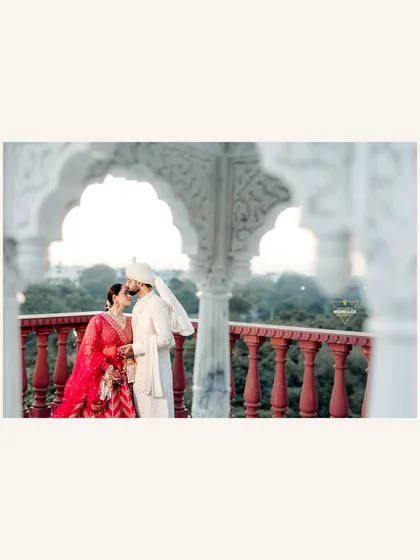 A beautifully framed shot of the couple sharing an intimate moment on a balcony with ornate white arches.
