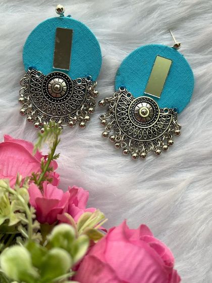 A fun and modern design. These round fabric earrings in a bright sky blue have a mirror accent and a large oxidised silver charm.