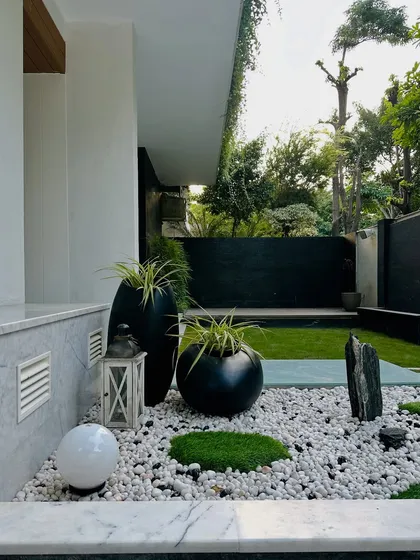 The same Zen garden, with a spherical light and a rustic lantern adding elements for evening ambiance. The contrast between the smooth white pebbles and the dark, rugged stones is a key feature.