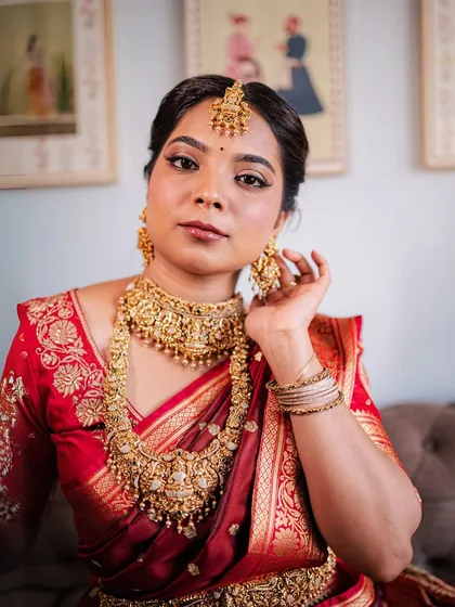 A close-up of a bride in a red silk saree, her look elevated by an intricate temple jewellery set. The craftsmanship is designed to make you feel like a goddess.