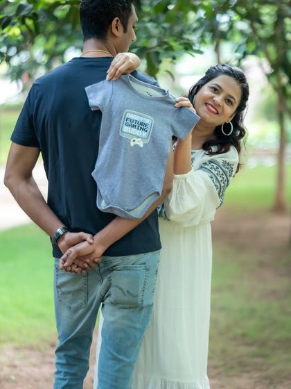 A cute announcement photo where the mom-to-be holds a "Future Gamer" onesie, with her partner's back to the camera.