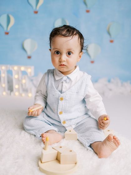 A close-up of a baby boy in a charming outfit against a handmade blue sky backdrop. The details in the setup add a touch of magic.
