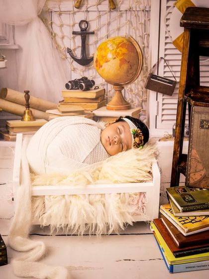 Adventure awaits this little dreamer. Our sailor-themed newborn shoot features a baby sleeping in a tiny bed surrounded by books, a globe, and nautical props for a whimsical touch.