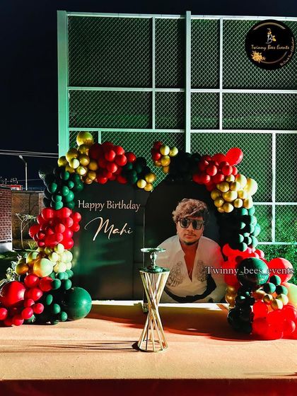 A bold and stylish birthday setup for Mahi. We used a dark green backdrop with his photo and a red, green, and gold balloon arch to create a powerful and personalized look.