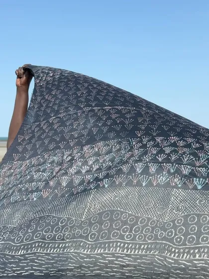 A finished indigo sari from our Bábbarra x Tharangini collaboration, featuring designs by Deborah Wurrkidj and Janet Marawarr. The textile, titled 'Kunred dja Kundalk' (Country and Grasses), blows in the sea breeze at Ndjudda point in Australia.