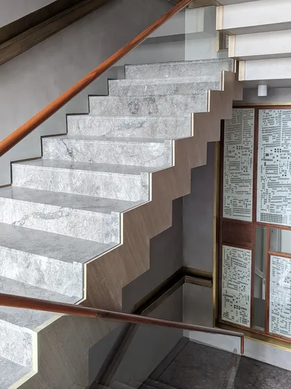 A detail of the marble steps and custom wooden handrail of the main staircase at the Bammi Residence. The design emphasizes clean lines and the natural beauty of the materials, creating a sense of understated luxury.