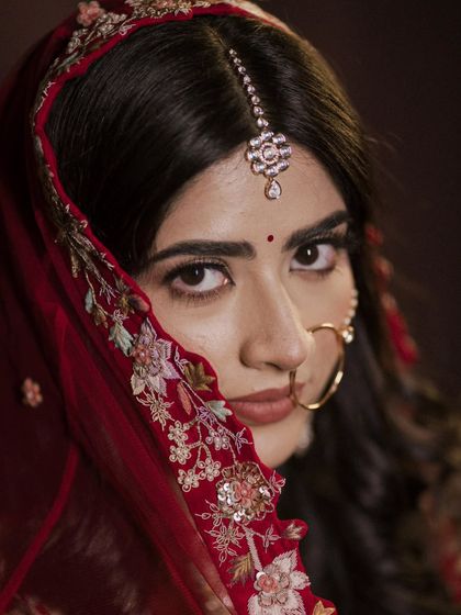An intense and beautiful close-up of the bride, Anisha. Her direct gaze and the details of her makeup and maang tikka are stunningly captured.