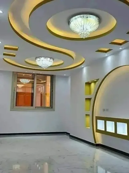 I specialize in creating complex, curved designs with gypsum. This living room features a flowing false ceiling with integrated chandeliers and cove lighting, which continues down into a custom-built wall unit with illuminated display niches.