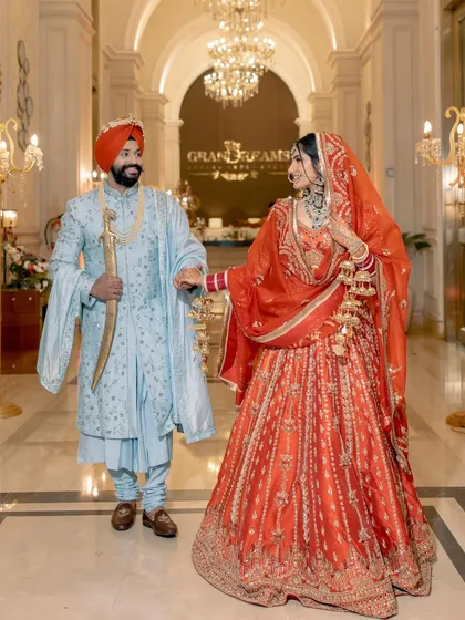 The couple walks hand-in-hand through a grand, beautifully lit corridor, their regal outfits perfectly matching the luxurious venue.