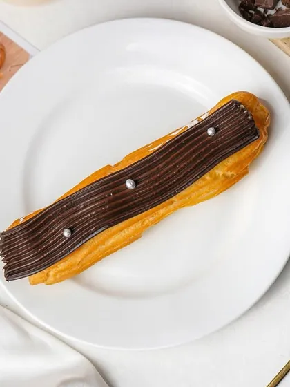 A single chocolate eclair on a white plate, shot from above. This clean, minimalist photo is perfect for showcasing individual pastries with elegance.