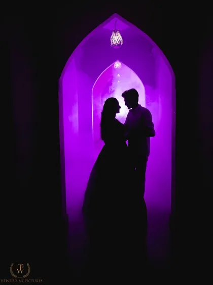 A dramatic silhouette of a couple framed by an archway filled with vibrant purple smoke. This shot demonstrates our creative approach, using props and lighting to create moody, artistic pre-wedding portraits.