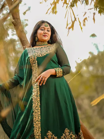 An artistic, low-angle shot looking up at the model in her green Anarkali, framed by golden leaves.