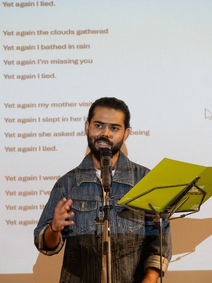A participant performs his piece at the 'Verse & Voice' showcase, with his poem projected behind him. Our workshops focus on both writing and stage performance skills.