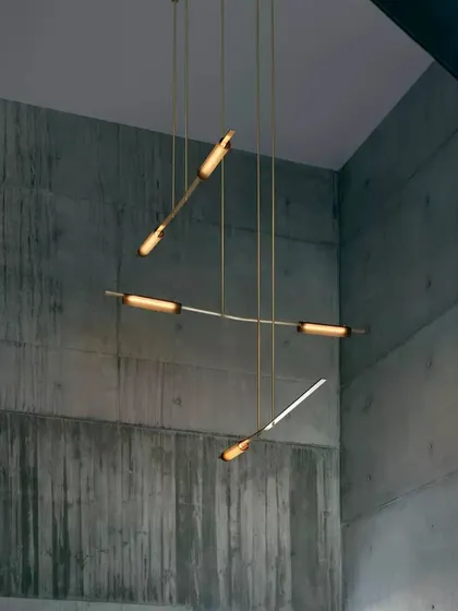The Volant chandelier in a raw, concrete space. The warm brass and soft light provide a beautiful contrast to the industrial texture of the walls.