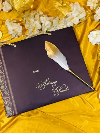 A sophisticated carry-bag style invitation in a deep aubergine, with the couple's names in elegant gold script and a traditional patterned border.
