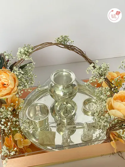 A detailed look at the silver puja thali set, complete with a diya, bell, and containers, all arranged on a tray with fresh flowers.