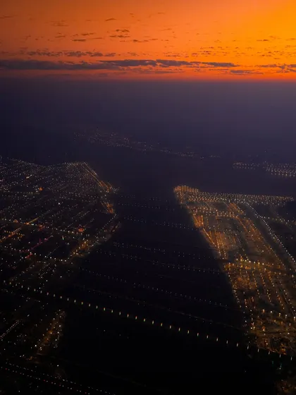 An abstract aerial photograph of Prayagraj during the Mahakumbh Mela at night. The city lights stretch across the landscape, hinting at the massive scale of the world's largest religious gathering.