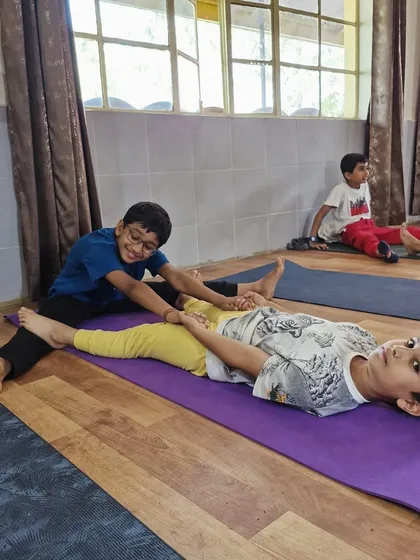 "Help thy neighbor as thy self." Two boys work together in a partner stretch, learning the importance of cooperation and gentle assistance in their yoga practice.