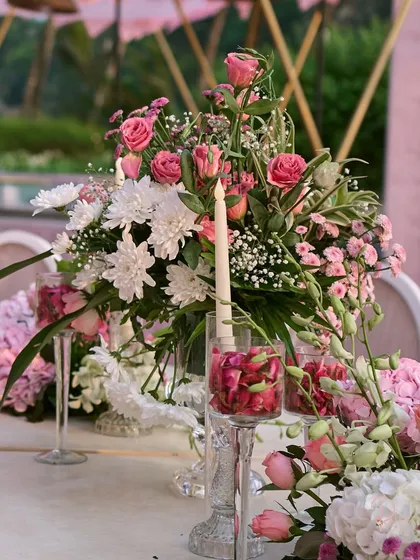 A close-up of a table centerpiece, showing the mix of pink roses, white chrysanthemums, and delicate baby's breath, paired with a single elegant candle.