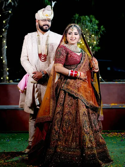 A full-length portrait of the bride and groom in their wedding attire, captured outdoors at night.