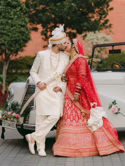 A classic romance with a touch of grandeur. Ambika and Sidhant share a joyful kiss by a vintage car, blending timeless style with the celebratory spirit of their wedding day. This shot shows how we can incorporate unique elements to make your couple portraits truly unforgettable.