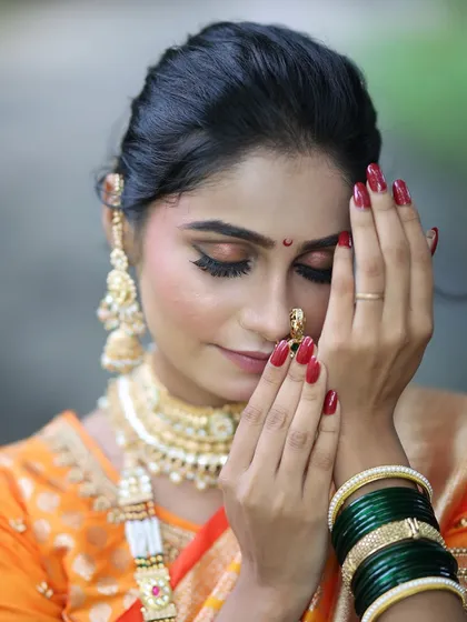 A close-up shot focusing on the soft, shimmery eye makeup and the traditional nath. The red nails add a perfect finishing touch to the bridal look.