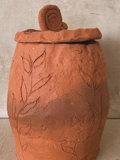 A lidded terracotta jar with delicate leaf patterns etched into the surface.