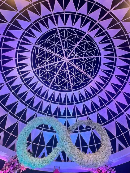 The ceiling of the 'Anant' dome, featuring the Flower of Life pattern, with the floral infinity symbol suspended below. This detail represents the couple's eternal journey beginning under a sacred sky.