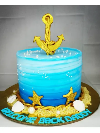 A "Welcome Back Daddy" cake for a merchant navy officer. This fresh pineapple cake has an ocean theme with a golden anchor, shells, and a beautiful blue ombre effect.