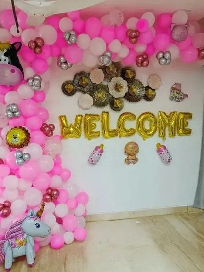 A welcome decoration for a baby, featuring pink balloons and unicorn and cow character foils.