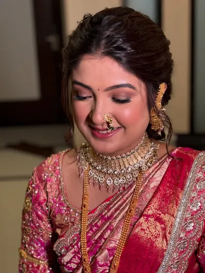 A candid moment of a smiling bride. Her makeup features a soft pink eyeshadow to match her saree, glowing cheeks, and a traditional 'nath' that highlights her Maharashtrian heritage.