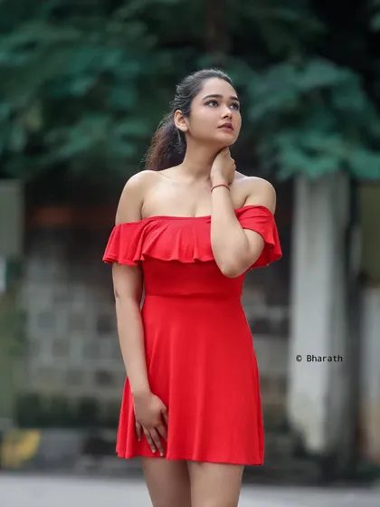A beautiful outdoor portrait of a model in a bright red off-the-shoulder dress. The soft, natural light and blurred background create a romantic and elegant feel.