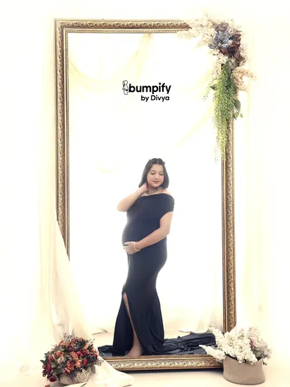 A creative and artistic portrait using a large, ornate mirror frame. The mom-to-be in a classic black gown is perfectly framed, creating a picture within a picture.