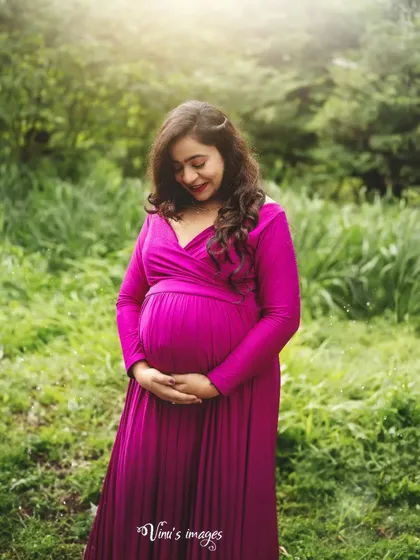 A close-up portrait capturing the mother's serene expression as she looks down at her bump. The lush green background enhances the feeling of life and nature.