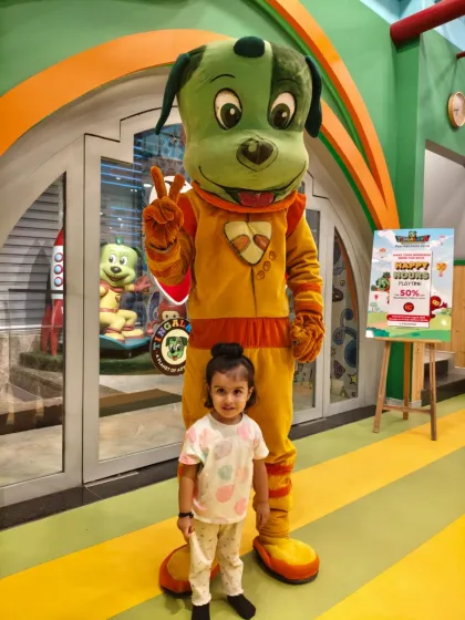 A little girl stands confidently next to the tall Tinga Dojo mascot, ready for her adventure to begin.