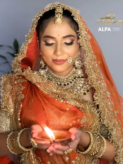 Holding a diya, the warm light accentuates the glow of the highlighter and the richness of the bridal attire.