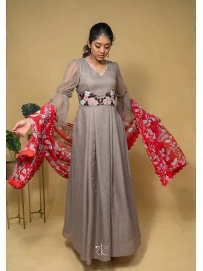 This mud brown net georgette dress offers a rustic yet chic charm. The look is elevated by a vibrant red floral scalloped dupatta.