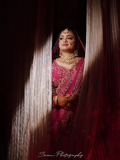 A beautiful bridal portrait, capturing the bride peeking through curtains with soft light illuminating her face.