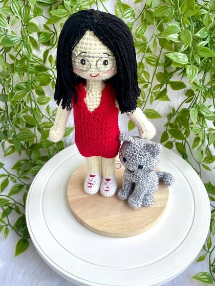 A thoughtful farewell gift for a niece heading off to higher studies. This replica doll in a red dress stands with her pet cat on a display base, a reminder of home she can take with her.