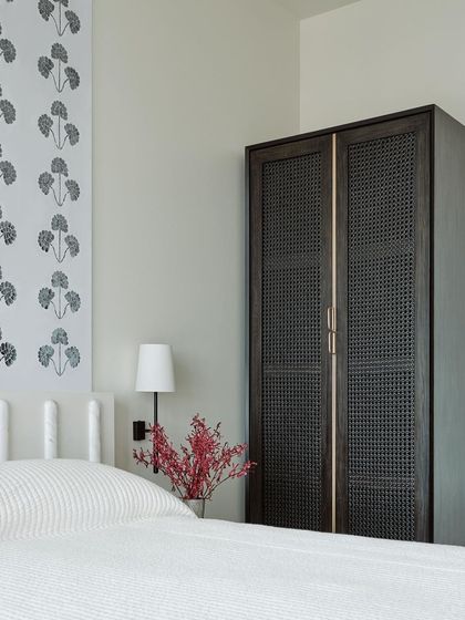 The finished Thikri panel installed as a headboard feature in a guest bedroom. Paired with a simple white headboard and a dark-stained cane wardrobe, the intricate glasswork becomes the room's quiet, elegant centerpiece.