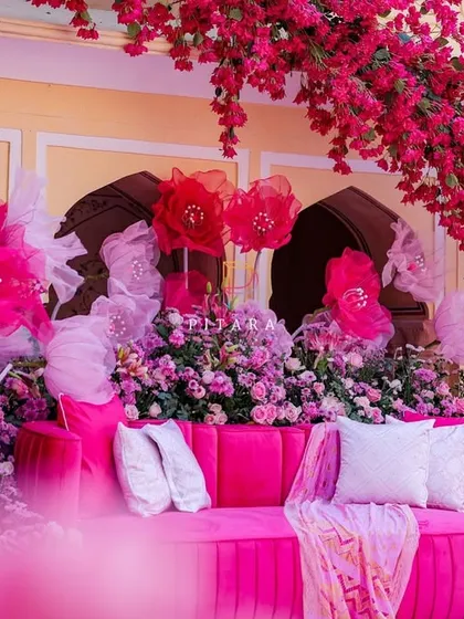 A close-up of the main photo stage, where the pink velvet sofa is nestled among an explosion of flowers and whimsical, oversized paper blooms. The details here are what make the setup truly special.