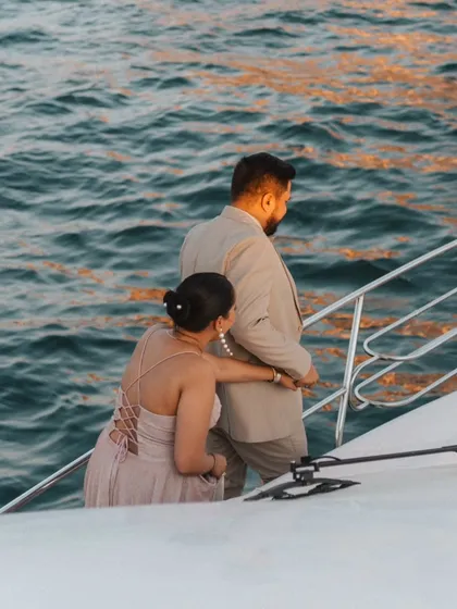 A candid shot of the couple on their private yacht, looking out at the ocean together as the sun sets, creating a romantic and cinematic feel.