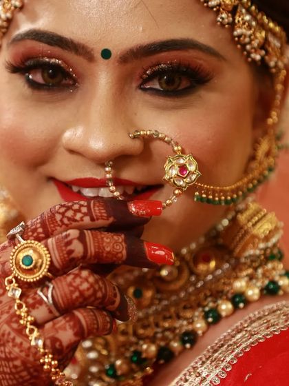 A close-up of a bride's stunning makeup and jewelry. Her hand, adorned with my mehndi, delicately touches her nose ring, highlighting the intricate details.