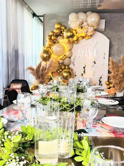 An elegant Aqeeqa ceremony featuring a glamorous tablescape and a stunning backdrop of gold and white balloons with pampas grass.