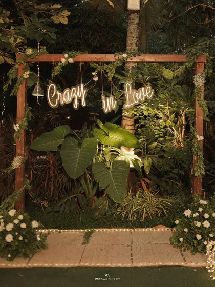 A fun and modern touch for a reception: a "Crazy in Love" neon sign nestled within a frame of natural greenery and white flowers, creating the perfect photo opportunity.