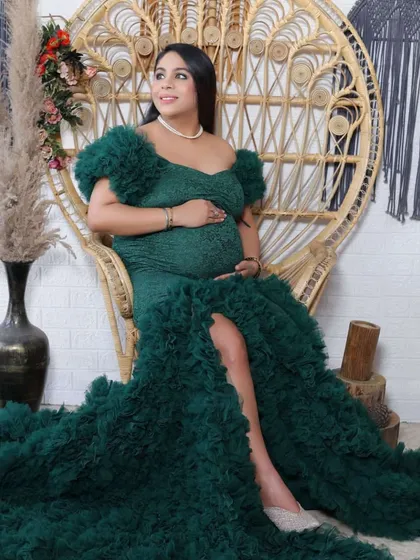 A regal portrait of a mother-to-be in a textured green ruffled gown, seated on a wicker peacock chair. We use props like this to add a touch of elegance.