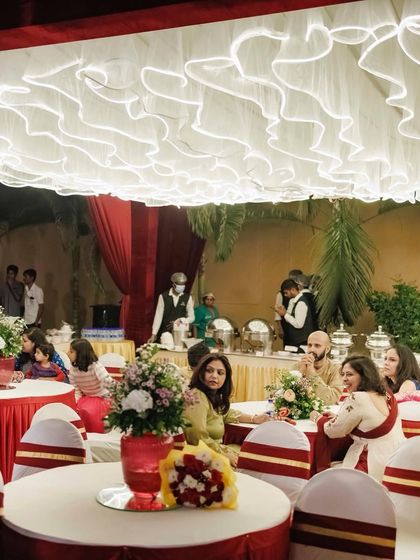 A glimpse of the guest seating at an indoor reception. The ruffled ceiling drapes and classic red and white table settings create an elegant and timeless atmosphere for the dinner celebration.