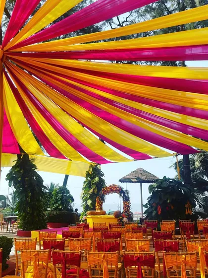 A colorful canopy of pink and yellow drapes set against the beach. This Haldi setup is bright, cheerful, and perfect for a fun-filled celebration by the sea.